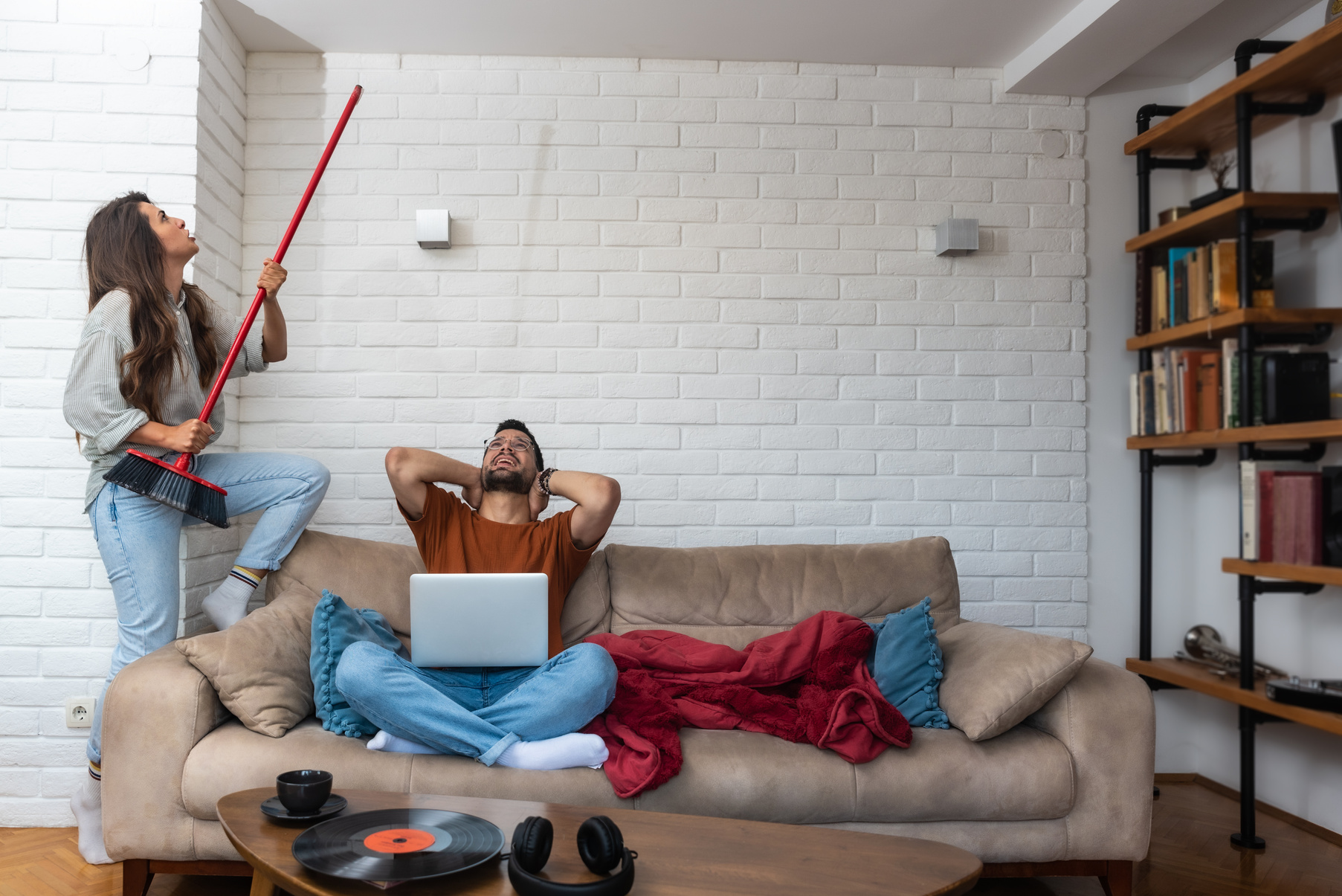 Young couple stares at the ceiling and yells because a neighbor upstairs is having a party with loud music or renovating an apartment and workers are drilling with heavy tools. Noise pollution concept